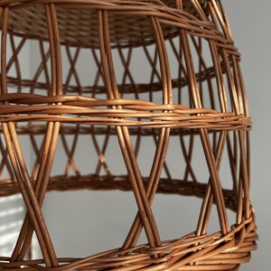 May include: A woven wicker lampshade with a natural brown color. The lampshade is made of thin, interwoven strips of wicker, creating a delicate and airy design.