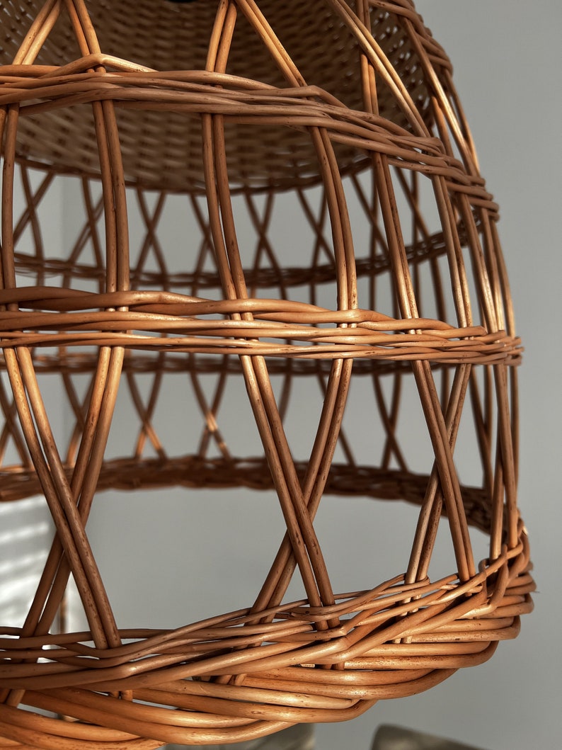 May include: A woven wicker lampshade with a natural brown color. The lampshade is made of thin, interwoven strips of wicker, creating a delicate and airy design.