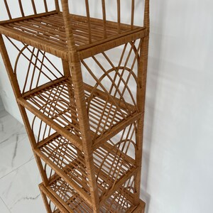 May include: A tall, natural woven wicker shelf unit with five shelves. The shelf unit has a rounded top and a woven design.