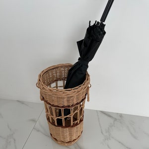 Pu&ograve; includere: Un portaombrelli in vimini con un ombrello nero all'interno. Il portaombrelli &egrave; fatto di vimini intrecciato con uno schema di colori marrone e naturale.