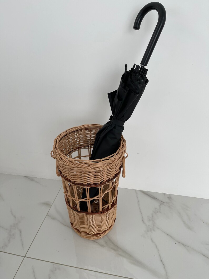 Pu&ograve; includere: Un portaombrelli in vimini con un ombrello nero all'interno. Il portaombrelli &egrave; fatto di vimini intrecciato con uno schema di colori marrone e naturale.