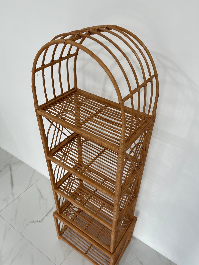 May include: A tall, natural woven rattan shelf unit with four shelves and an arched top. The shelf unit is made of light brown rattan and has a natural finish.