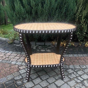 May include: A brown wicker end table with a white trim. The table has two shelves and is sitting on a stone patio.