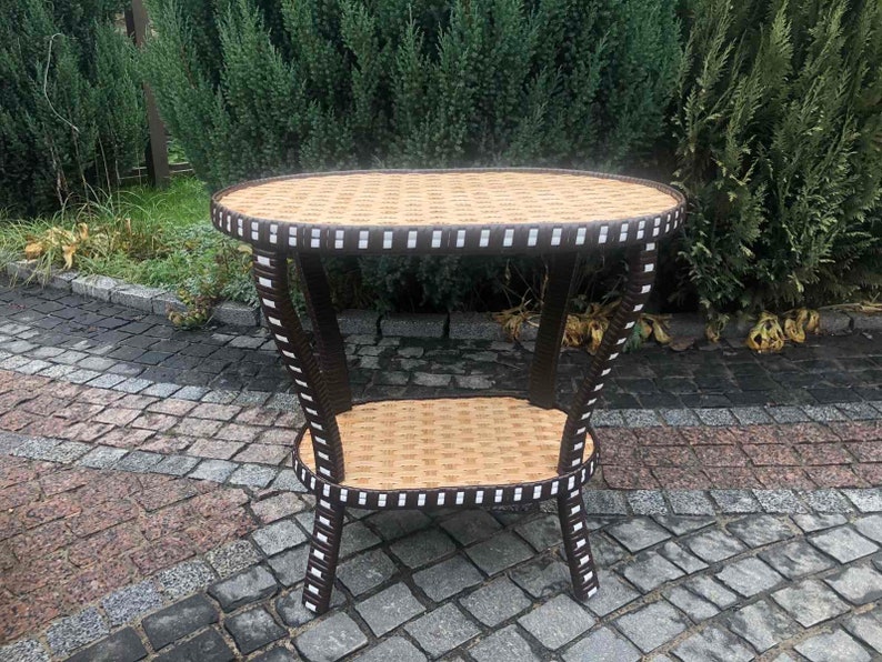 May include: A brown wicker end table with a white trim. The table has two shelves and is sitting on a stone patio.