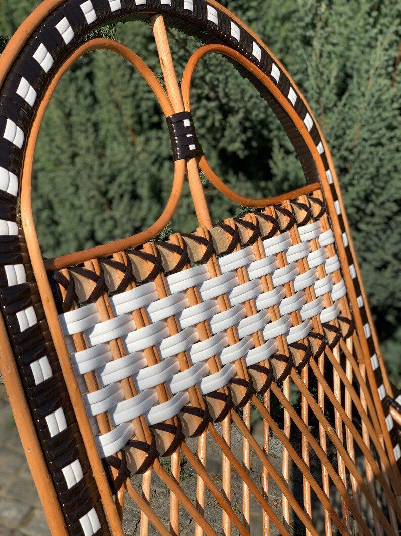 May include: A brown wicker chair with a white and black woven seat and back. The chair has a black and white geometric pattern around the top and sides.