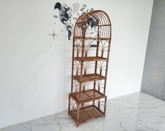 May include: A brown wicker shelf unit with four shelves and a curved top. The shelf unit is standing on a white tiled floor.