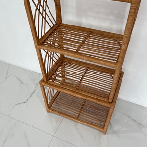 May include: A four-tiered woven rattan shelf unit with a natural brown finish. The shelf unit is made of woven rattan and has a rectangular shape.