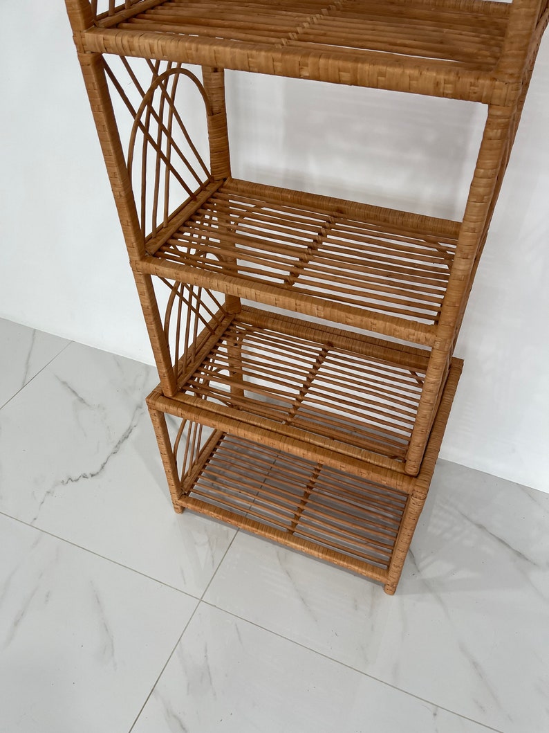 May include: A four-tiered woven rattan shelf unit with a natural brown finish. The shelf unit is made of woven rattan and has a rectangular shape.