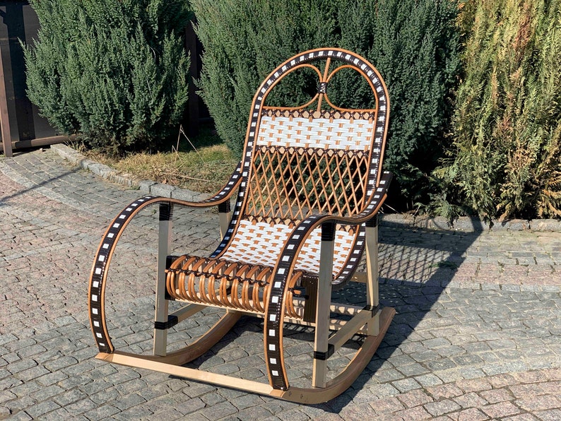 May include: A brown and white wicker rocking chair with black and white trim. The chair is on a patio with a brick walkway.