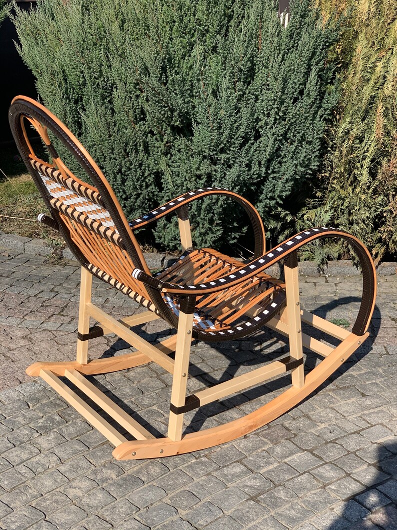 May include: A wooden rocking chair with a woven seat and back. The chair is painted brown and has black accents. The chair is sitting on a patio.