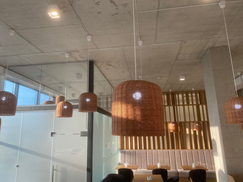 Puede incluir: Un interior de cafeter&iacute;a moderno con un techo de hormig&oacute;n y una fila de l&aacute;mparas colgantes tejidas que cuelgan sobre un banco rosa con paredes de listones de madera. La cafeter&iacute;a tiene una pared de vidrio con una puerta de vidrio esmerilado y una ventana con vista al cielo.