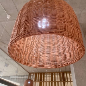 Puede incluir: Una l&aacute;mpara colgante de mimbre tejido de color marr&oacute;n natural. La luz cuelga de un cable blanco e ilumina la habitaci&oacute;n.