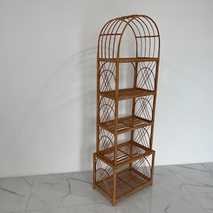 May include: A tall, arched, woven rattan shelf unit with four shelves. The shelf unit is made of natural brown rattan and has a geometric design.
