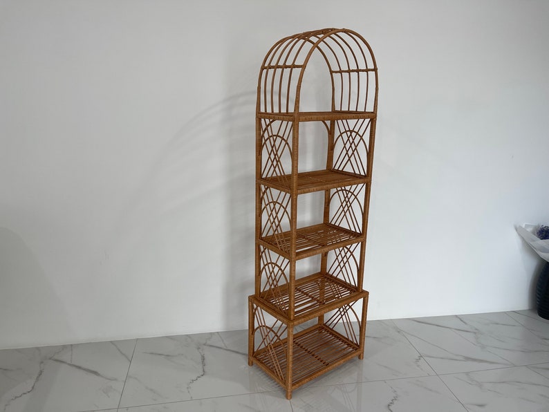 May include: A tall, arched, woven rattan shelf unit with four shelves. The shelf unit is made of natural brown rattan and has a geometric design.