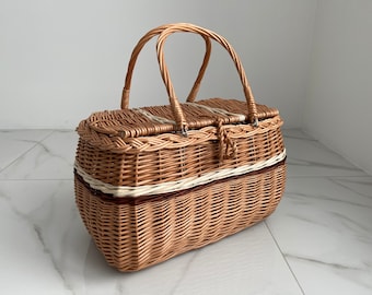 May include: Woven wicker picnic basket with a hinged lid and two arched handles. The basket features a light brown color with white and dark brown accents. The basket is designed with a clasp closure.