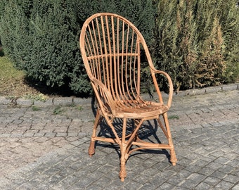 Op de afbeelding: Een gevlochten rieten stoel met een hoge rugleuning en armleuningen. De stoel is gemaakt van natuurlijke bruine riet en heeft een licht gebogen rugleuning.
