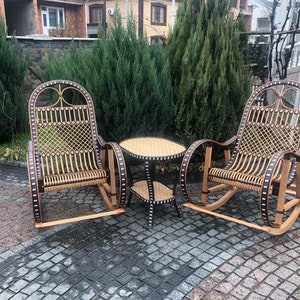 May include: Two wicker rocking chairs with black accents and a small round wicker table with a black top. The chairs and table are on a gray brick patio.