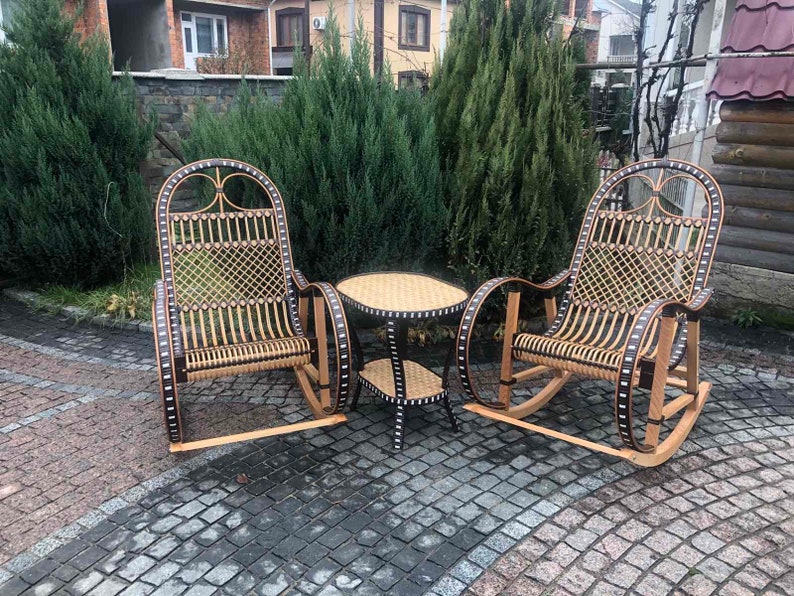 May include: Two wicker rocking chairs with black accents and a small round wicker table with a black top. The chairs and table are on a gray brick patio.