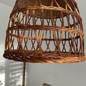 May include: A woven wicker pendant light fixture with a natural brown color. The light fixture is made of thin, interwoven strips of wicker, creating a delicate and airy design.