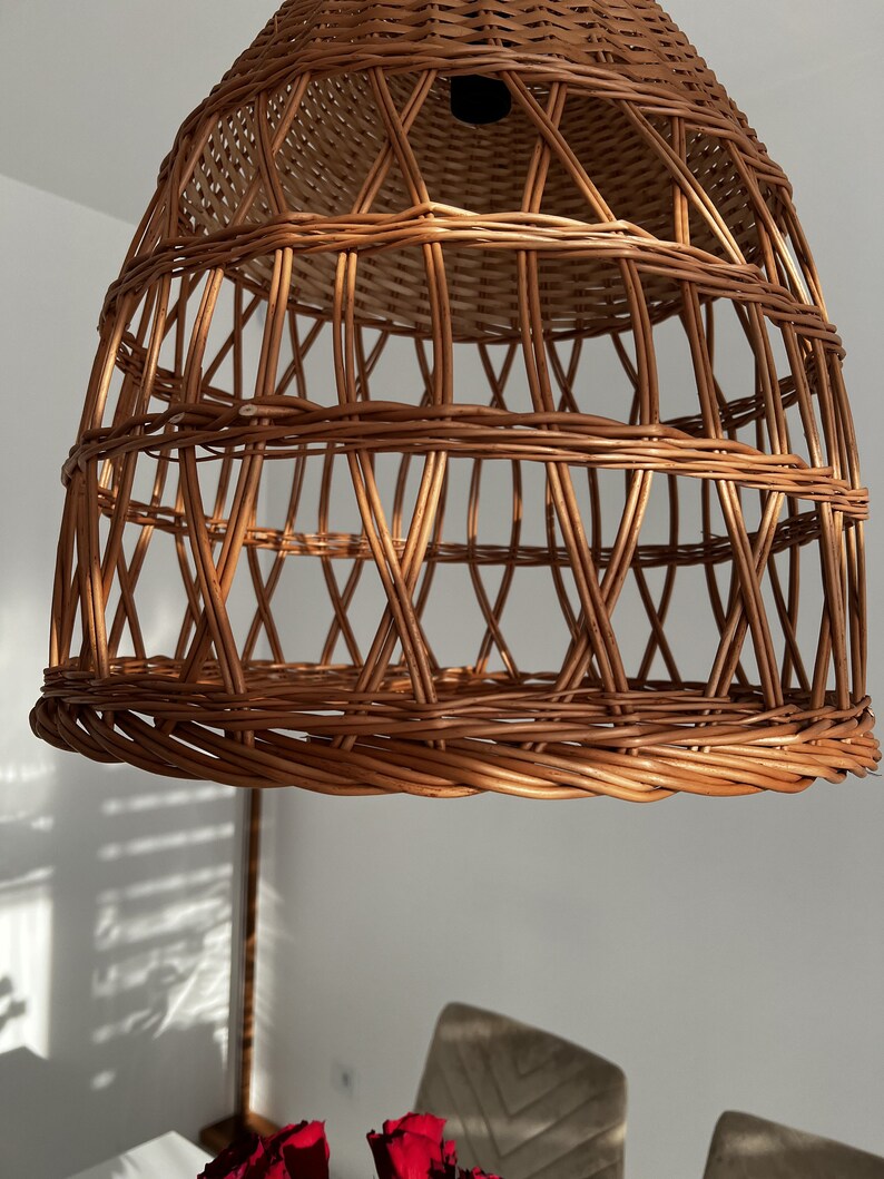 May include: A woven wicker pendant light fixture with a natural brown color. The light fixture is made of thin, interwoven strips of wicker, creating a delicate and airy design.