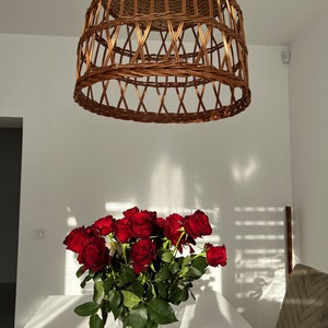 May include: A bouquet of deep red roses in a clear glass vase on a white table. The roses are in focus, while the background is blurred. A wicker lampshade hangs from the ceiling above the table.