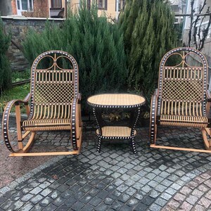 May include: Two wicker rocking chairs with black accents and a small wicker table with a black top. The chairs and table are on a gray stone patio.