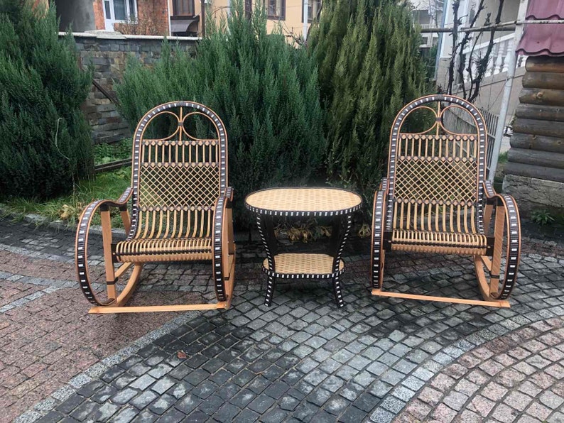 May include: Two wicker rocking chairs with black accents and a small wicker table with a black top. The chairs and table are on a gray stone patio.