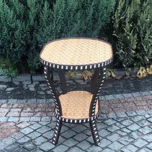 May include: A brown wicker end table with a white trim and two shelves. The table is sitting on a gray cobblestone patio.