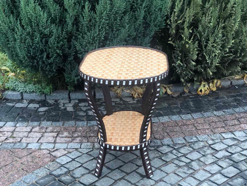 May include: A brown wicker end table with a white trim and two shelves. The table is sitting on a gray cobblestone patio.