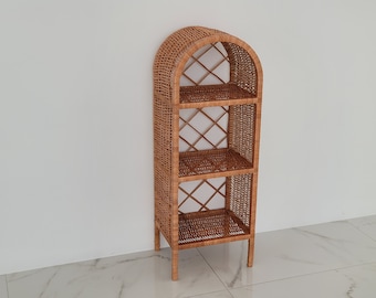 May include: A three-tiered wicker shelf with an arched top. The shelf is made of natural woven wicker and has a light brown color.