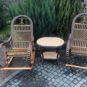 May include: A set of two wicker rocking chairs with black accents and a matching wicker table with a black top. The chairs and table are on a gray stone patio.