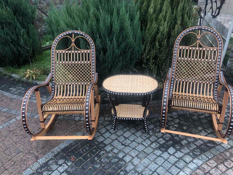 May include: A set of two wicker rocking chairs with black accents and a matching wicker table with a black top. The chairs and table are on a gray stone patio.