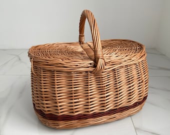 May include: A woven wicker picnic basket with a brown handle and a brown stripe around the bottom.