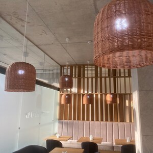 Puede incluir: Un interior de restaurante moderno con una zona de asientos de banqueta rosa claro y una pared de listones de madera. El restaurante tiene un dise&ntilde;o minimalista con sillas negras y mesas de madera. El techo tiene varias l&aacute;mparas colgantes de mimbre.