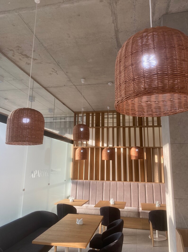 Puede incluir: Un interior de restaurante moderno con una zona de asientos de banqueta rosa claro y una pared de listones de madera. El restaurante tiene un dise&ntilde;o minimalista con sillas negras y mesas de madera. El techo tiene varias l&aacute;mparas colgantes de mimbre.
