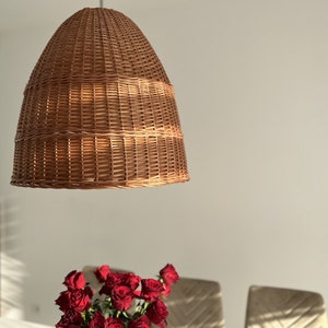 Może przedstawiać: Wisząca lampa z brązowego wikliny, wisząca z sufitu. Lampa wykonana jest z plecionej wikliny i ma okrągły, kopułowy kształt.