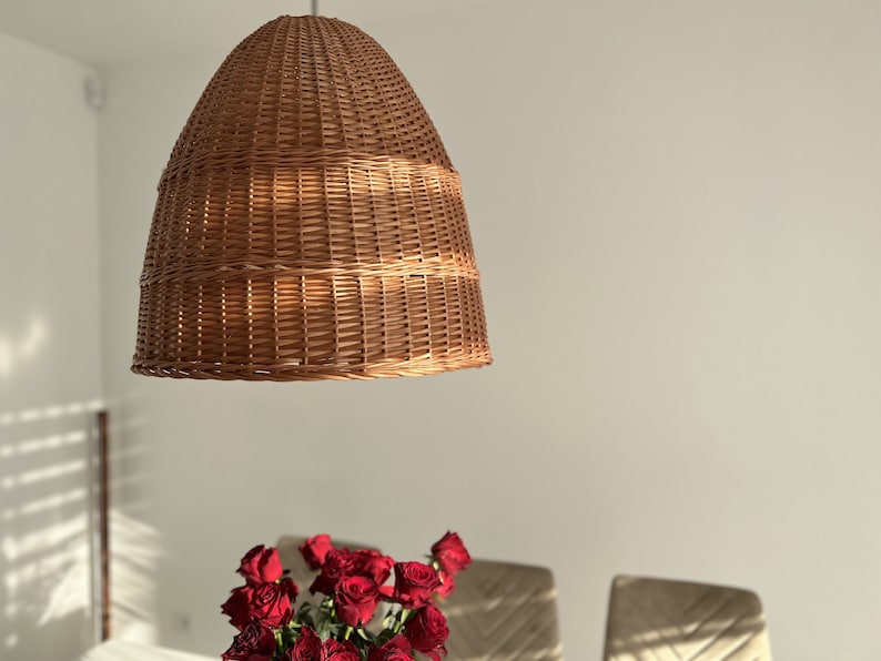Może przedstawiać: Wisząca lampa z brązowego wikliny, wisząca z sufitu. Lampa wykonana jest z plecionej wikliny i ma okrągły, kopułowy kształt.