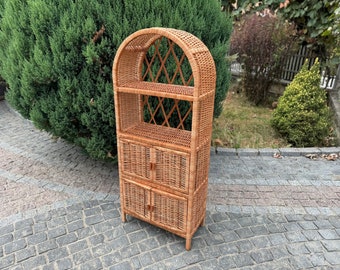 May include: A natural wicker shelf unit with an arched top and two doors. The shelf has two open shelves and two closed shelves with doors.