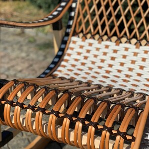 May include: A close-up of a rocking chair with a woven seat and back. The seat is made of brown and black wicker, and the back is made of white and brown wicker.