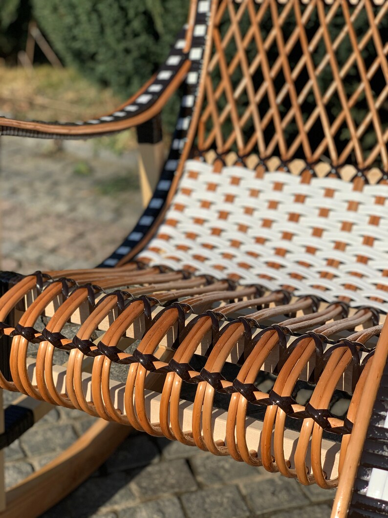 May include: A close-up of a rocking chair with a woven seat and back. The seat is made of brown and black wicker, and the back is made of white and brown wicker.