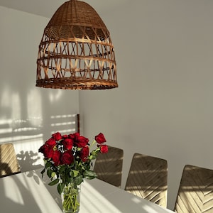 May include: A white table with a wicker pendant light hanging above it. A bouquet of red roses in a clear glass vase sits on the table. There are six brown velvet chairs around the table.