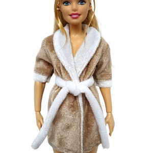 May include: A brown plush robe with a white trim and a white tie belt. The robe is worn by a doll with blonde hair and blue eyes.
