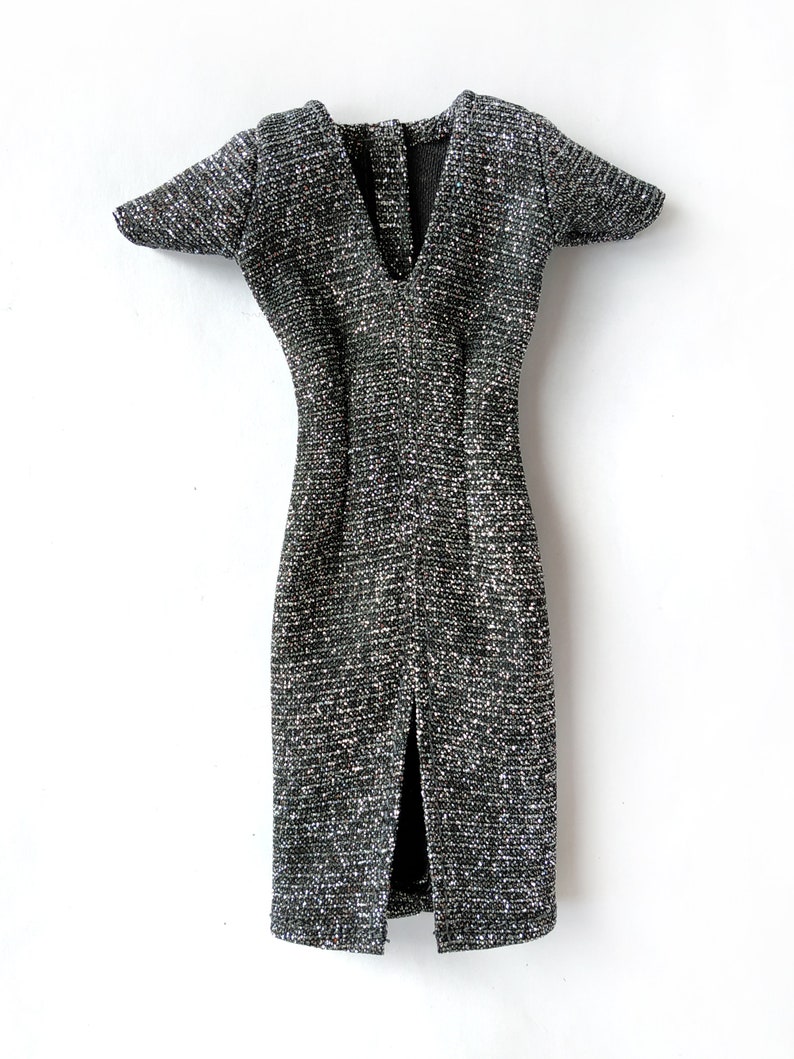 Puede incluir: Un vestido plateado y negro brillante con cuello en V y mangas cortas. El vestido tiene una abertura en la parte delantera y una silueta ajustada.