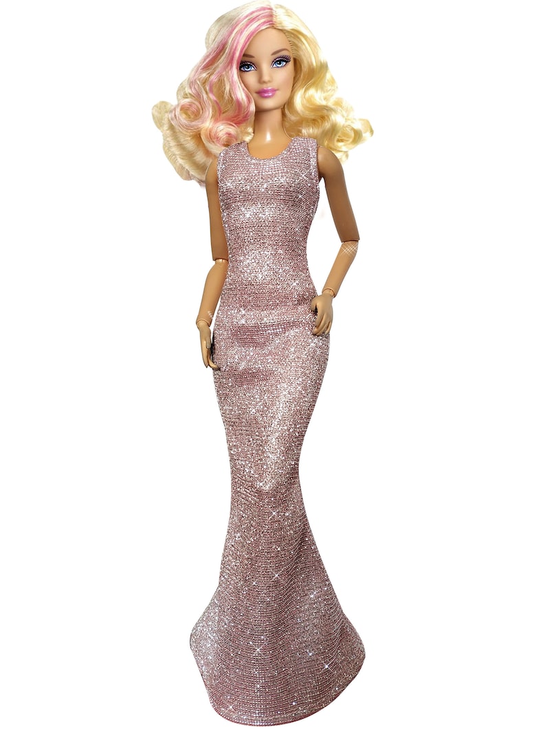 May include: A fashion doll with blonde hair, highlighted with pink streaks, and blue eyes. The doll is wearing a shimmering, rose-colored gown. The dress is floor-length and has a fitted bodice that flares out at the bottom.