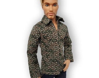 Puede incluir: Muñeco con una camisa abotonada de manga larga con un patrón geométrico en tonos verdes, marrones y grises. El muñeco también lleva pantalones azul oscuro. El muñeco tiene el pelo rubio y ojos azules.