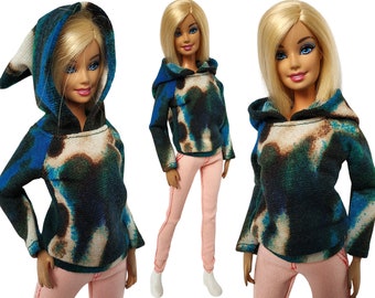 May include: Three dolls wearing a blue and green tie-dye hoodie with a white hood. The hoodie has a loose fit and long sleeves. The dolls are wearing pink pants.
