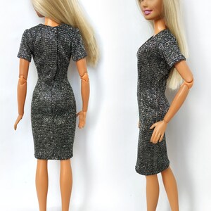 Puede incluir: Un vestido plateado brillante con mangas cortas y silueta ajustada. El vestido se muestra en una mu&ntilde;eca con cabello rubio.