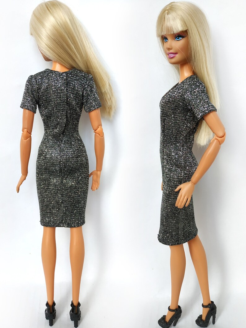 Puede incluir: Un vestido plateado brillante con mangas cortas y silueta ajustada. El vestido se muestra en una mu&ntilde;eca con cabello rubio.
