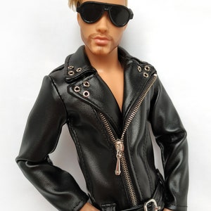 K&ouml;nnte beinhalten: Eine schwarze Lederjacke mit Rei&szlig;verschluss und G&uuml;rtel. Die Jacke hat einen silbernen Rei&szlig;verschluss und silberne Druckkn&ouml;pfe. Die Jacke wird von einer Puppe mit blonden Haaren und Sonnenbrille getragen.