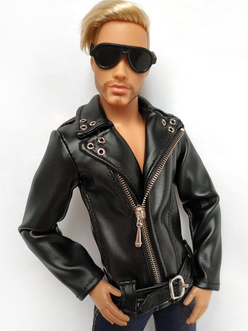 K&ouml;nnte beinhalten: Eine schwarze Lederjacke mit Rei&szlig;verschluss und G&uuml;rtel. Die Jacke hat einen silbernen Rei&szlig;verschluss und silberne Druckkn&ouml;pfe. Die Jacke wird von einer Puppe mit blonden Haaren und Sonnenbrille getragen.